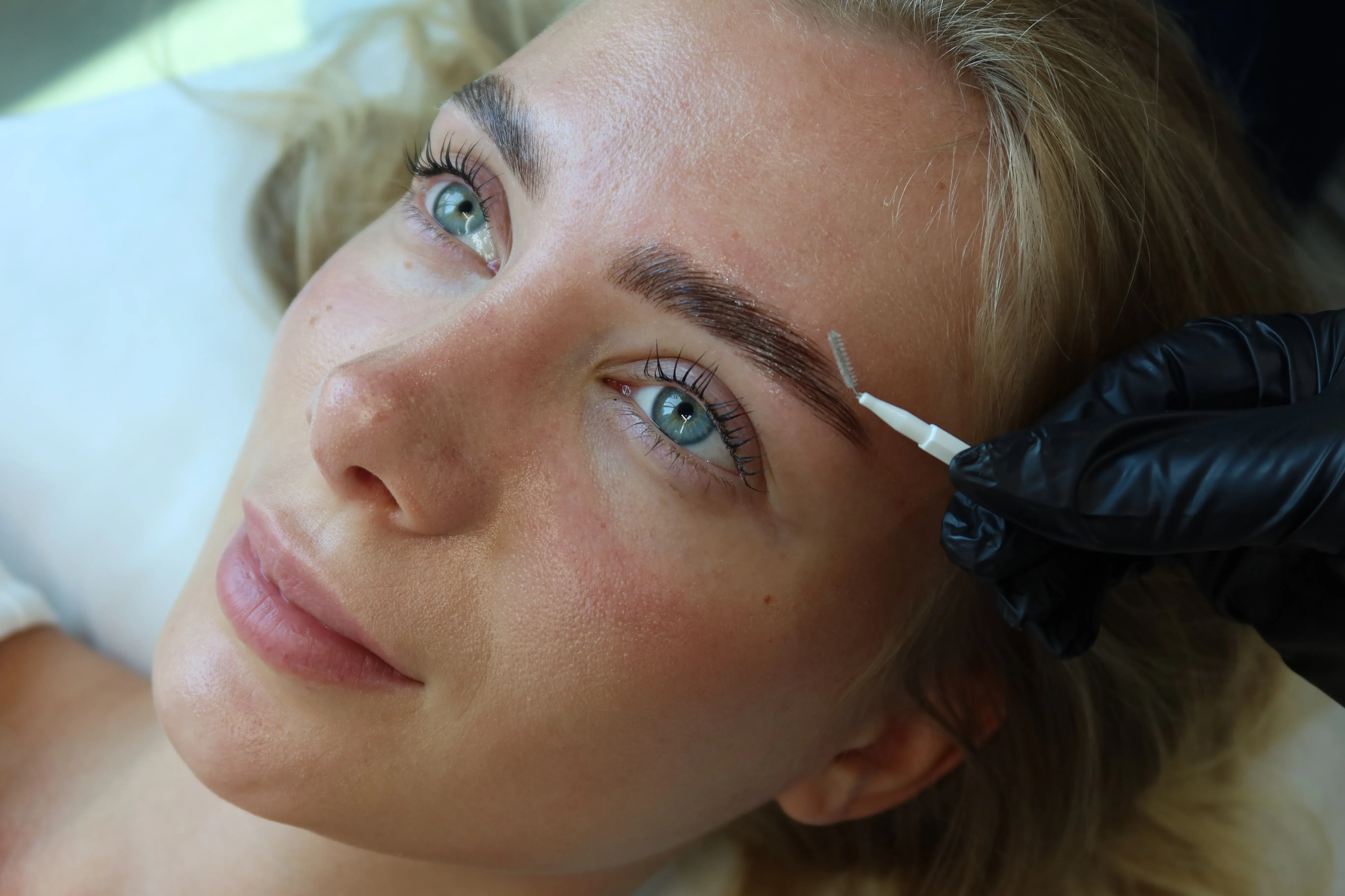 Azizam technician grooming a client's brows during a treatment